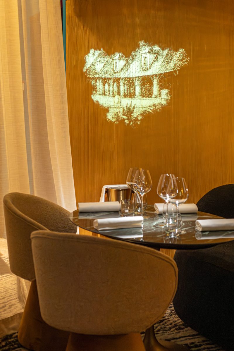 salle de Maison Joia Table dressée avec verres, chaises modernes et projection artistique sur un mur.