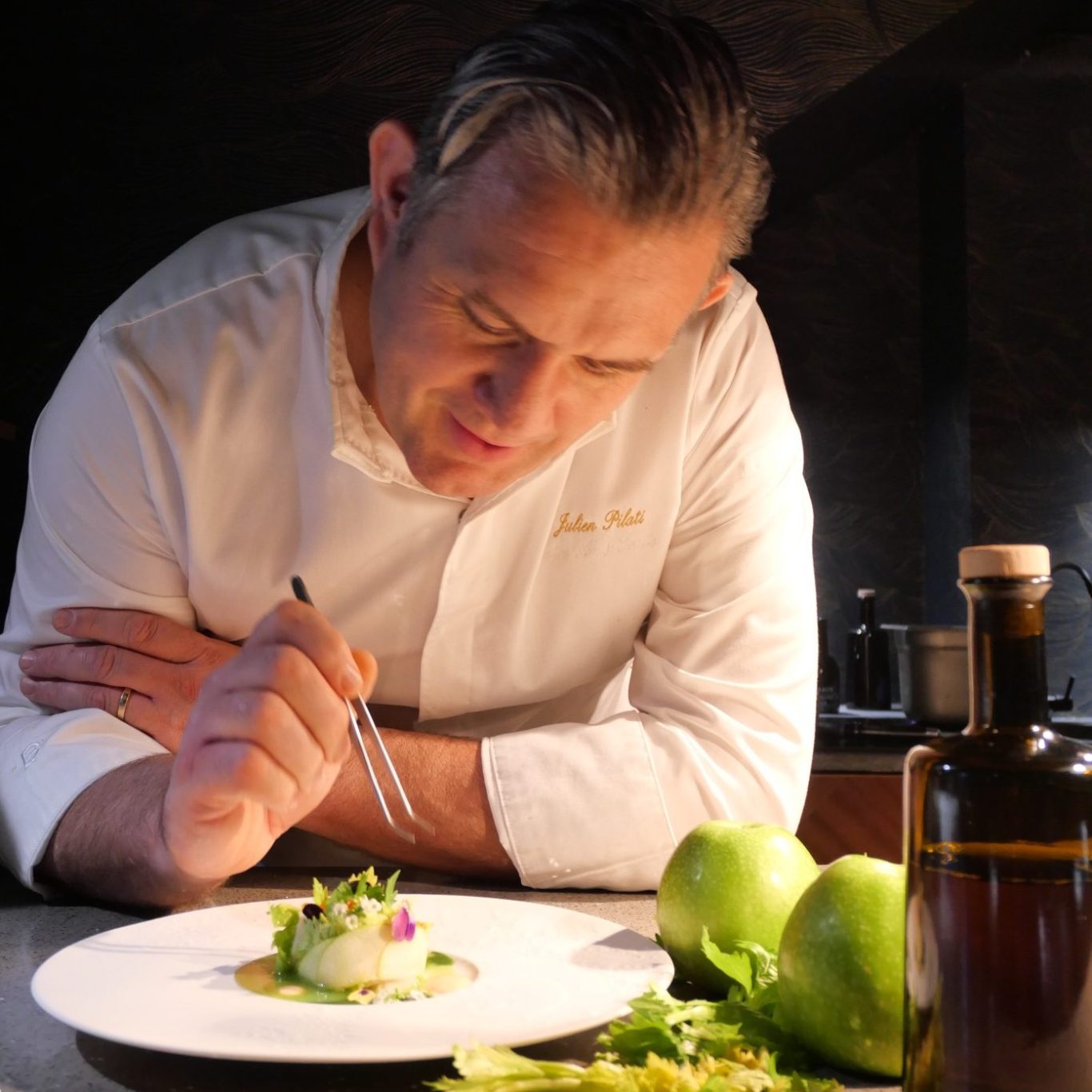 Le Chef Julien Pilati en pleine concentration, préparant un plat délicat avec des pommes vertes.
